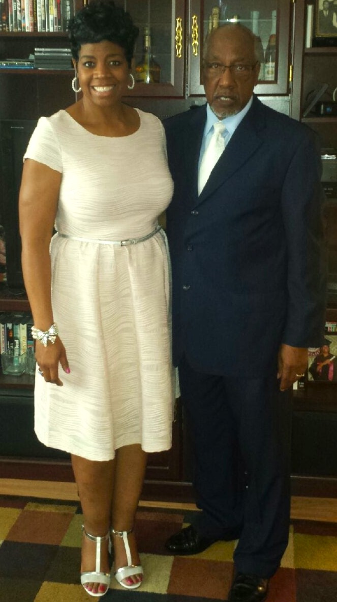 Rev. English in a navy suit standing with his daughter Deverri at home