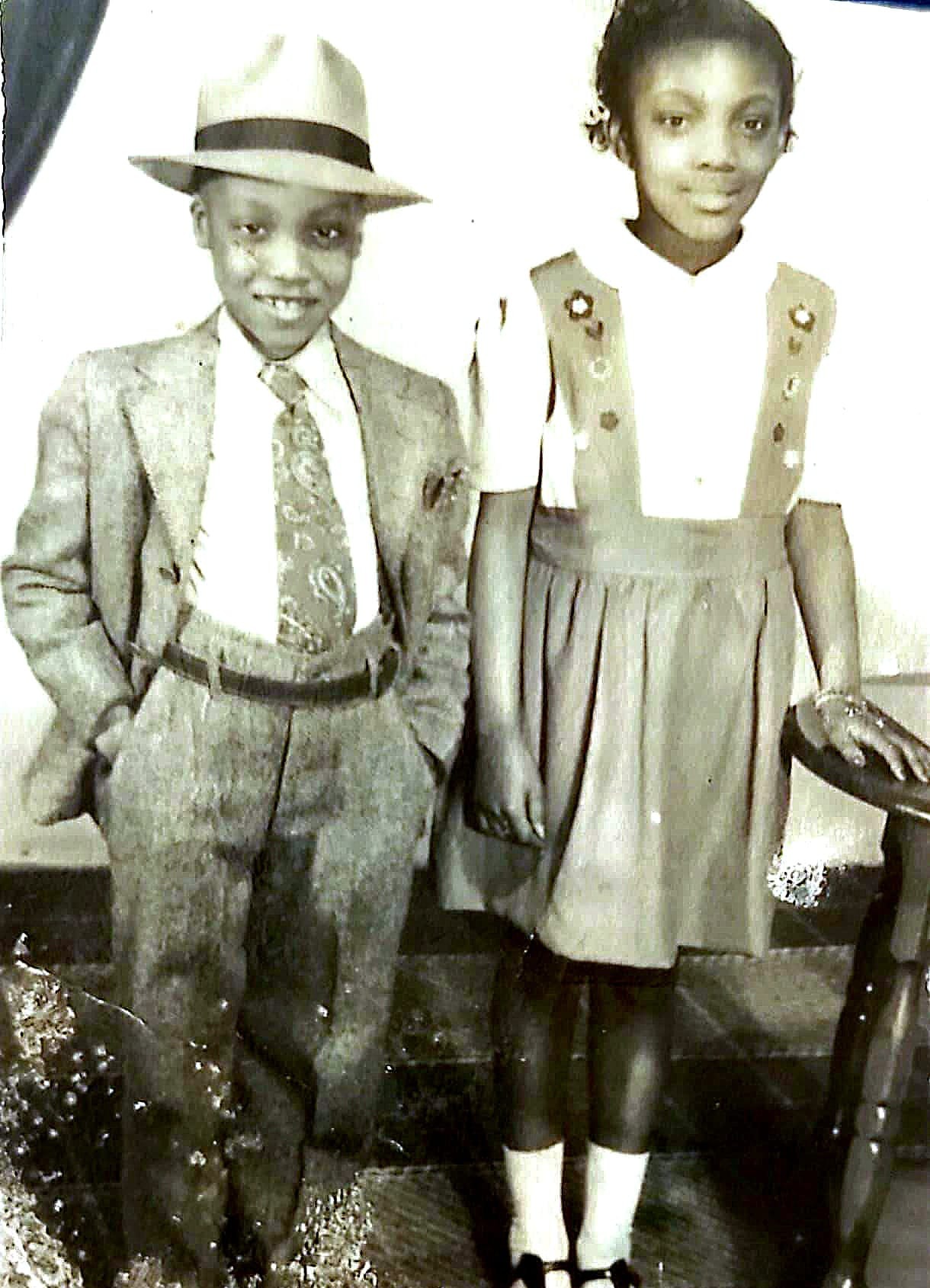 A young Ronald English in a suit, tie and fedora, standing beside his sister